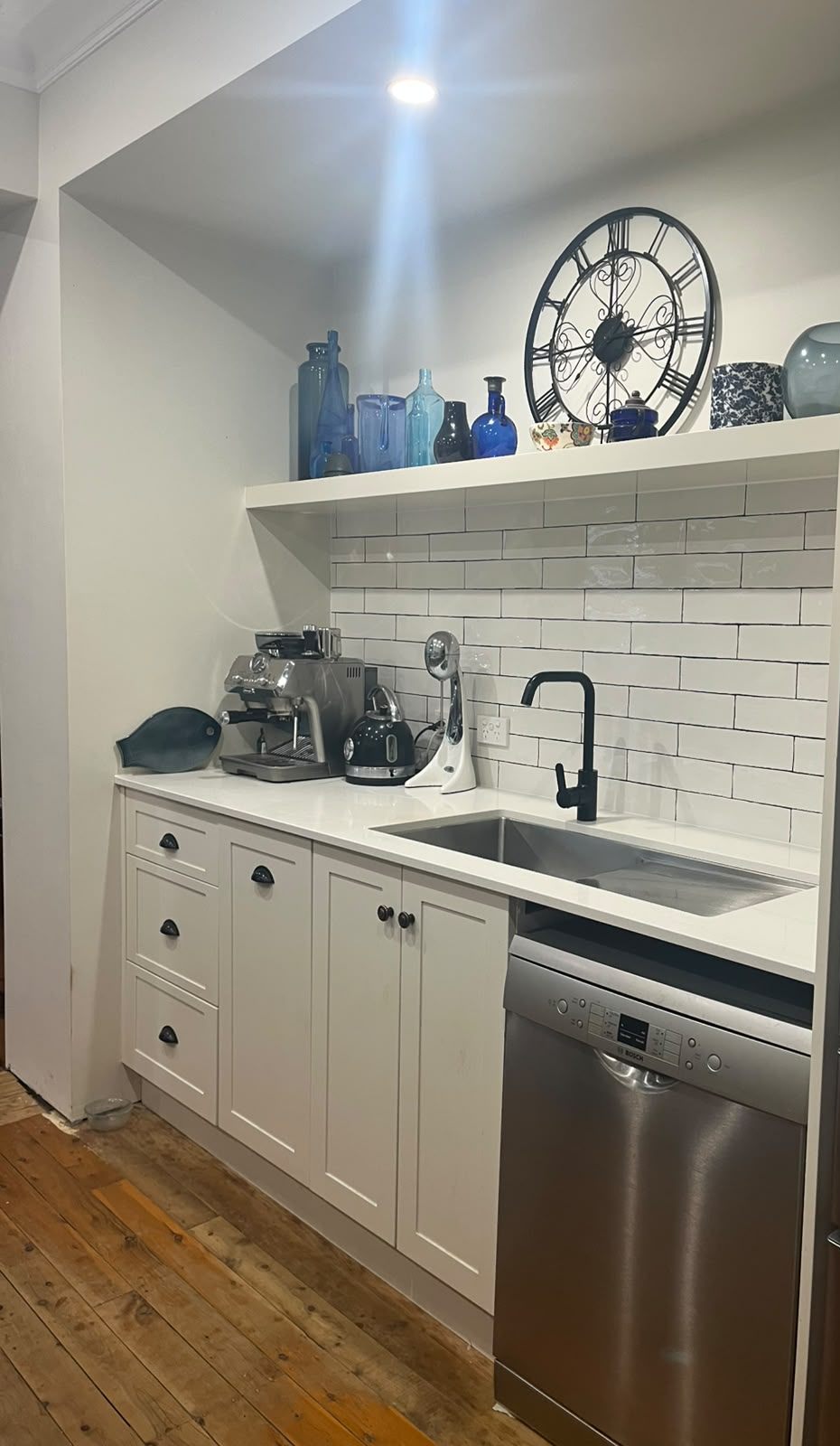 White shaker kitchenette with stone benchtop, subway tile splashback and floating shelf